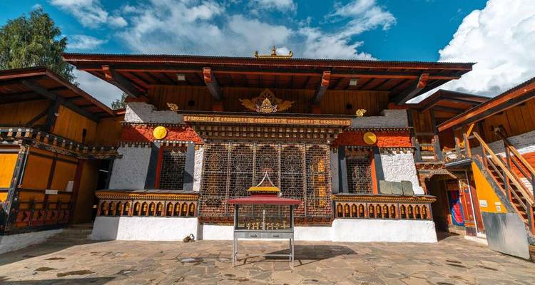 Frontansicht eines lebendigen bhutanischen Klosterhofs mit kunstvollen Holzarbeiten und bemalten Fassaden
