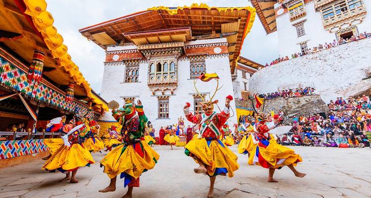 Lebendige maskierte Tänzer in gelben Kostümen führen ein traditionelles Fest im Hof einer Dzong auf, während eine große Menschenmenge zuschaut.