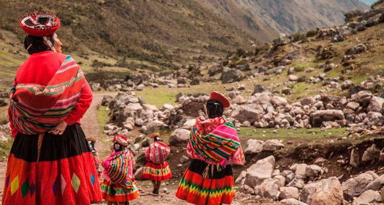 Des habitants vêtus de vêtements traditionnels aux couleurs éclatantes se tiennent le long d'un sentier andin rocheux surplombant une vallée