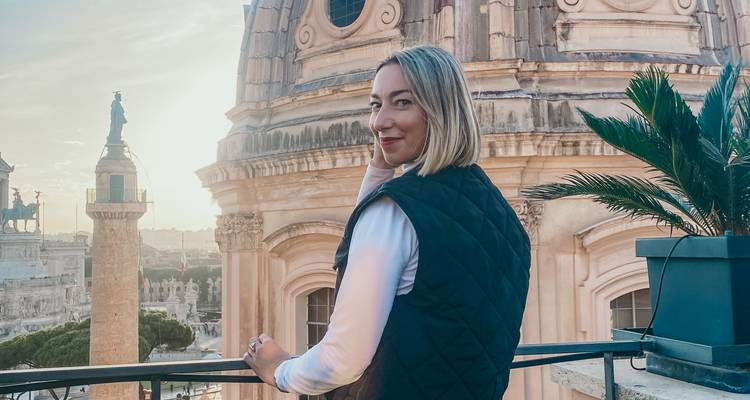 Jonge vrouw die poseert op een dakterras met Romeinse koepels en monumenten in het warme avondlicht.