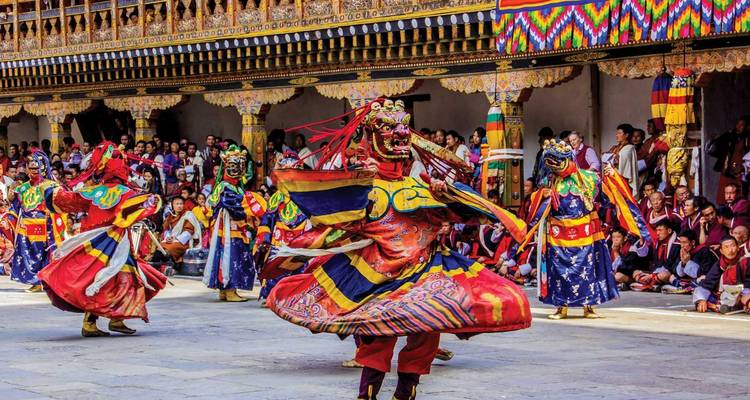 Colorful costumed dancers whirl during a Bhutanese festival inside an ornately decorated courtyard.