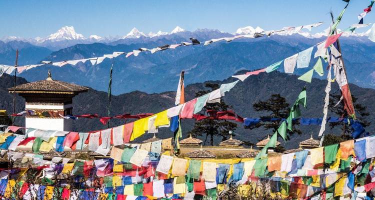 Colorful prayer flags flutter on a mountain pass with snowy Himalayan peaks in the distance.