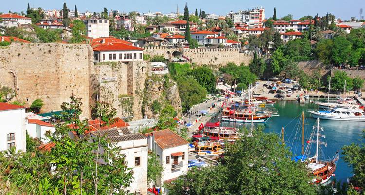 Des bateaux colorés bordent le vieux port d'Antalya sous les anciens murs de pierre et les quartiers verdoyants par une belle journée.