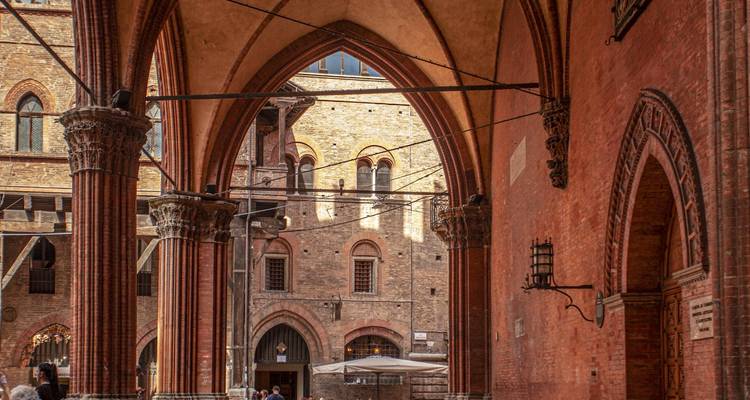 Les arches du gothique de brique encadrant la vue de la cour historique de Bologne avec des visiteurs se promenant