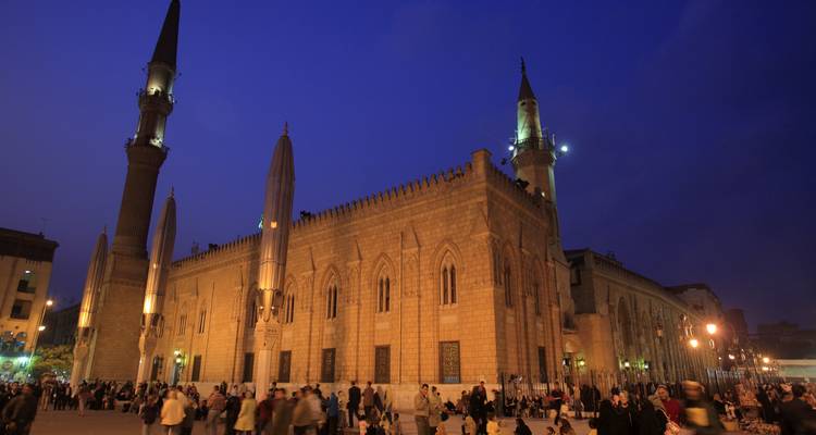 Las multitudes nocturnas se reúnen afuera de una mezquita histórica iluminada en el bullicioso centro de la ciudad de El Cairo.