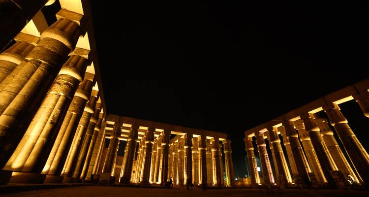 Los colonnades del Templo de Luxor iluminados de forma espectacular por la noche, creando largas sombras doradas contra el cielo oscuro.