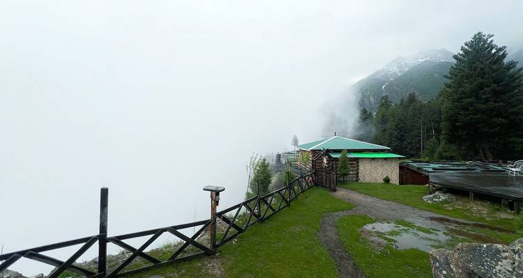 Una plataforma de observación se asoma a un valle perdido en espesa nube blanca, con senderos mojados y cercas de madera.