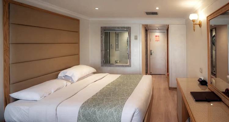 Cabine moderne et lumineuse de navire de croisière avec un grand lit double, des tons neutres et une fenêtre donnant sur la salle de bains attenante.