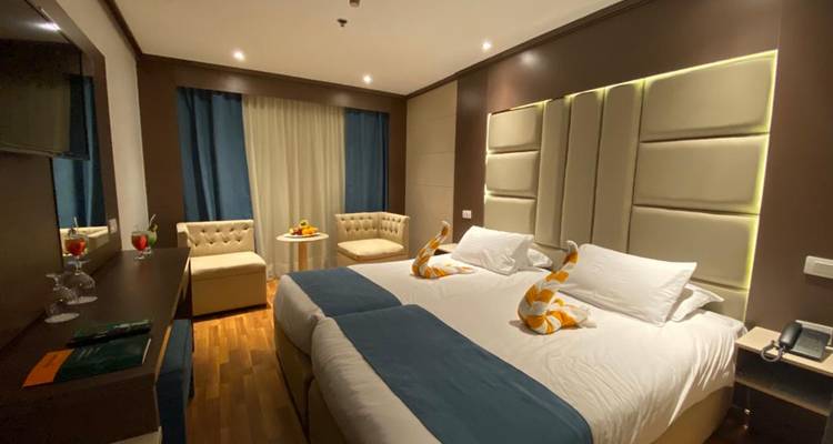 Suite élégante de navire de croisière avec deux lits jumeaux rapprochés, décorations de cygnes en serviettes et éclairage ambiant doux.
