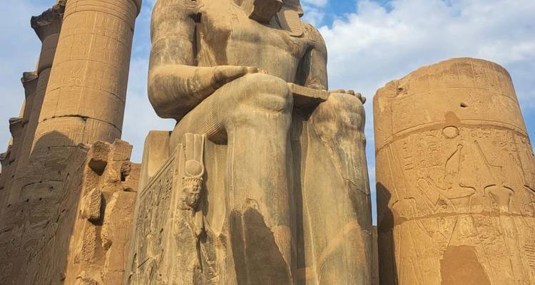 Une massive statue assise de Ramsès II domine la cour du temple de Louxor sous un ciel bleu.