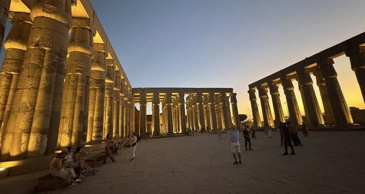 Cour du Temple de Louxor illuminée de lumières dorées au crépuscule, avec des visiteurs dispersés parmi les colonnes imposantes.