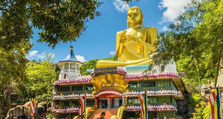 Massieve gouden Boeddha-standbeeld dat uittorent boven de kleurrijke gevel van het Golden Temple-complex onder een helder blauwe lucht.