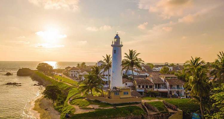Witte vuurtoren en koloniale gebouwen van Galle Fort verlicht door warm zonsondergangslicht.