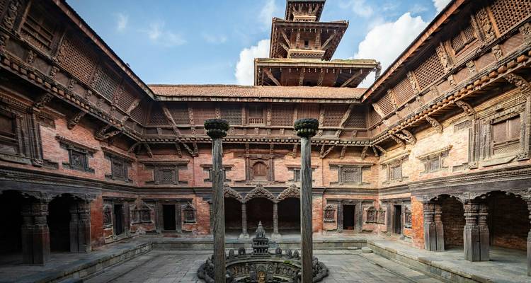 Patio intrincado de ladrillos y madera de un palacio tradicional Newari con ventanas talladas y pozo central.