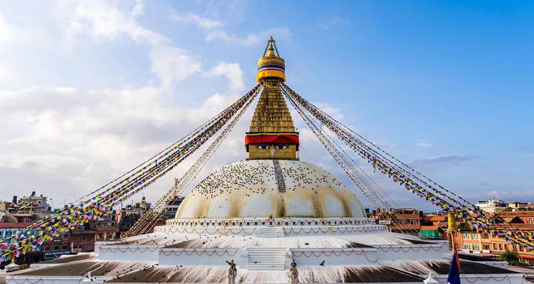 Cúpula encalada de la estupa de Boudhanath con coloridas banderas de oración extendiéndose hacia el cielo.