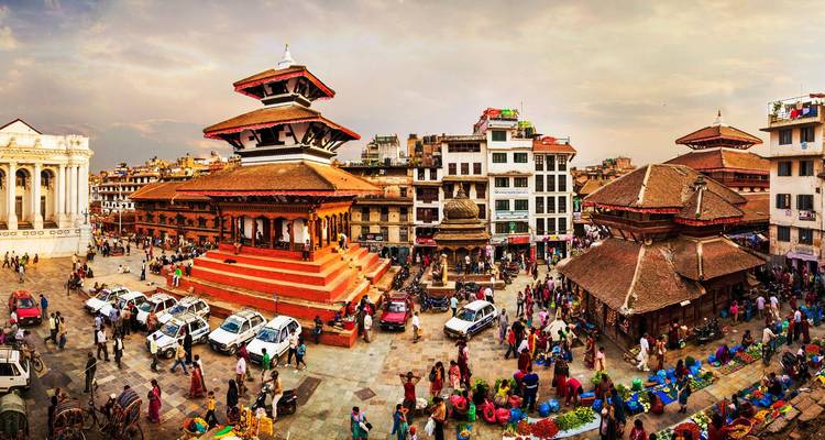 Vista panorámica de una plaza histórica llena de vida con templos pagoda de varios pisos de color rojo, edificios circundantes y multitudes de locales y visitantes.