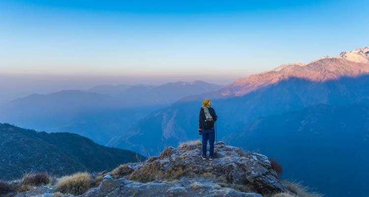 Un trekkeur en solo se tenant debout sur un sommet rocheux à l'aube, dominant les couches de montagnes de l'Himalaya.