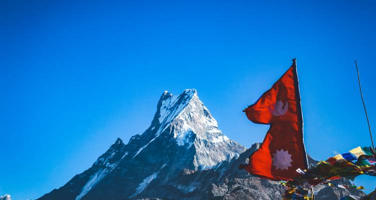 Pic emblématique de Machhapuchhare sur un ciel bleu profond avec le drapeau népalais et les drapeaux de prière en premier plan.