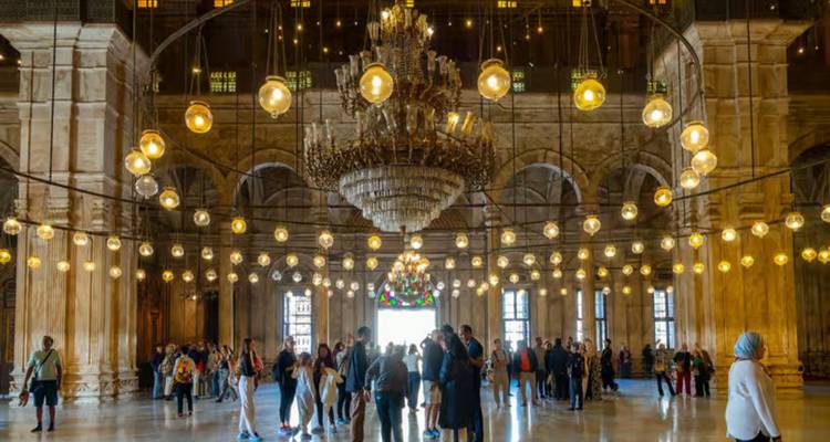 Interior de la Mezquita de Mohamed Ali con un gran candelabro y hileras de lámparas brillantes sobre los visitantes.