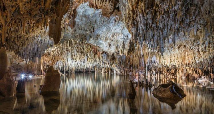 Grotte de calcaire remplie de stalactites se reflétant dans un lac souterrain immobile, doucement illuminé.