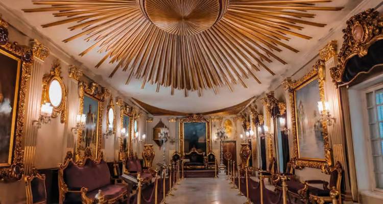Lujoso salón interior con marcos dorados, arañas de cristal y un espectacular techo con diseño de rayos de sol.