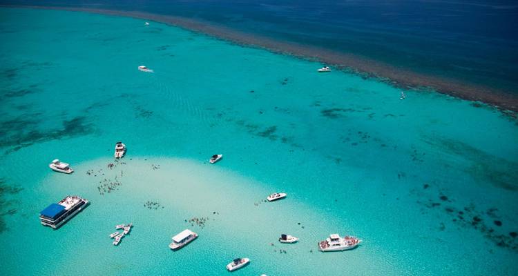 Vue aérienne de bateaux et de visiteurs rassemblés sur un banc de sable pâle dans une eau turquoise éclatante.