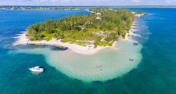 Vue aérienne d'un îlot couvert d'arbres avec de l'eau turquoise peu profonde environnante et un bateau ancré.