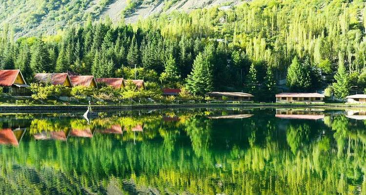 Rangée de cabines rustiques aux toits rouges se reflétant parfaitement dans le lac d'émeraude entouré de grands peupliers.