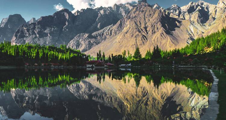 Les pics enneigés se reflètent nettement dans les eaux calmes du lac Shangrila encadrés par des pins et des chalets.