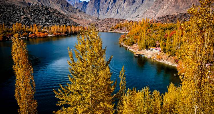 Des arbres d'automne éclatants bordent un lac bleu profond situé au milieu de collines rocheuses sous un ciel dégagé.