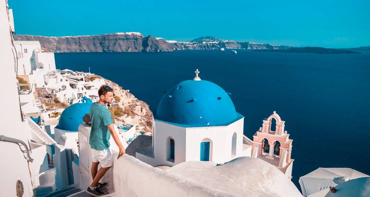 Reiziger in gestreept shirt geniet van het uitzicht op de blauwe koepels en caldeira van Santorini
