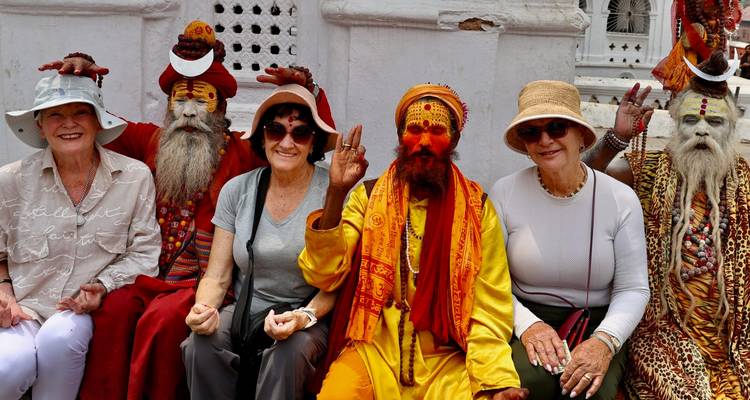 Des touristes assis avec des sadhus vêtus de robes aux couleurs éclatantes devant un sanctuaire blanchi à la chaux, souriant pour la caméra.