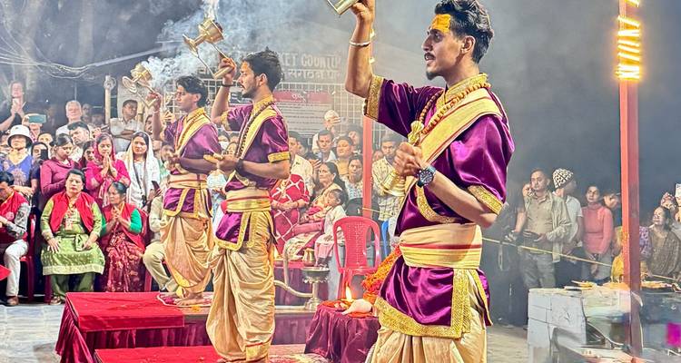 Cérémonie d'aarti en soirée avec trois prêtres vêtus de robes pourpres et dorées agitant l'encens devant un public nombreux.