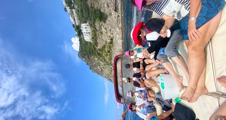 Un groupe de voyageurs se détend sur le pont d'un bateau rapide avec les falaises spectaculaires d'Amalfi s'élevant à l'arrière-plan.