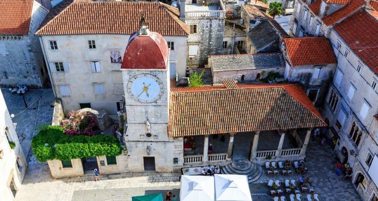 Historischer Uhrenturm und Ziegeldächer überblicken einen Steinplatz im mittelalterlichen Zentrum von Trogir