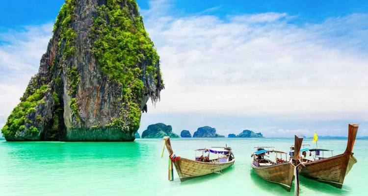 Mar tropical color turquesa con botes de cola larga tradicionales anclados junto a una imponente isla de piedra caliza verde tipo karst.