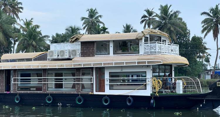Tradicional casa flotante de Kerala amarrada en las tranquilas aguas con palmeras de coco detrás.