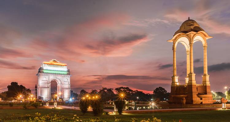 India Gate en het luifeldak van het monument gloeien tegen een levendige roze schemering met twinkelende lichtjes in de tuinen.