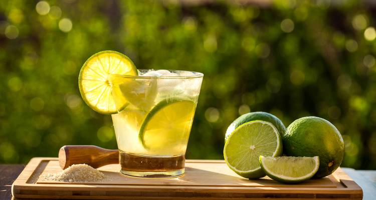Nahaufnahme eines erfrischenden Caipirinha-Cocktails mit frischen Limettenscheiben auf einem Holzbrett.