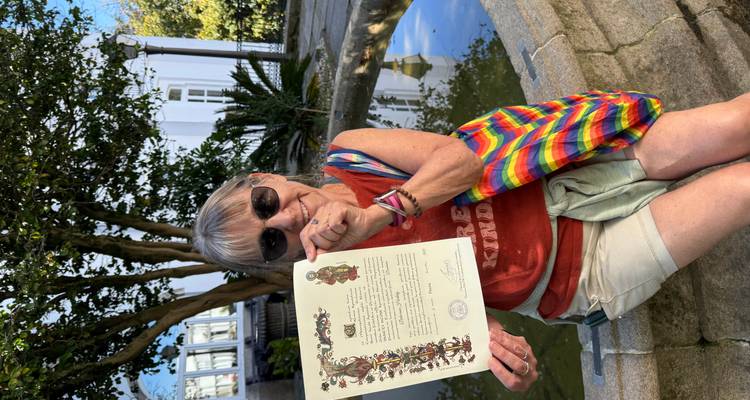 Une femme affiche fièrement un certificat en étant assise près d'une petite fontaine dans une cour verdoyante.