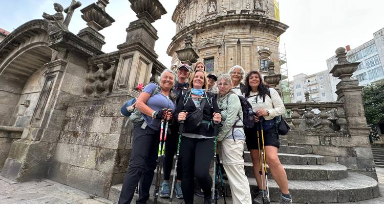 Un groupe de randonneurs pose avec des bâtons de trekking devant la façade ornée d'une église en pierre.