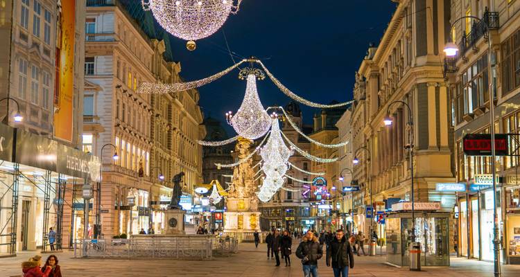 Weihnachtslichter und Kronleuchter hängen über Wiens Graben-Fußgängerzone mit abendlichen Einkäufern.