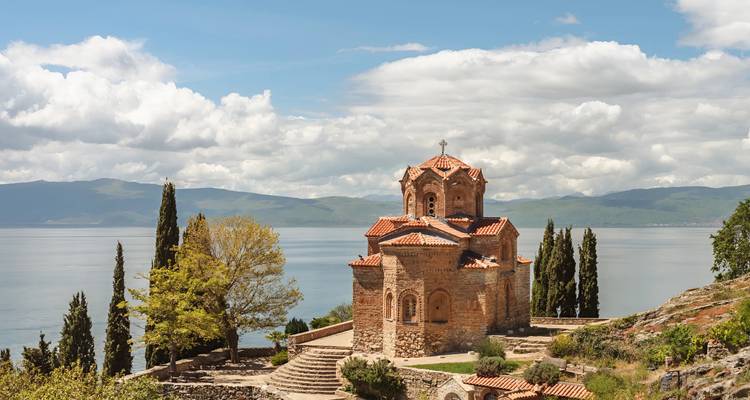La Iglesia de San Juan con tejado rojo en Kaneo se encarama sobre las aguas azul cristalino del Lago Ohrid bajo nubes esponjosas.
