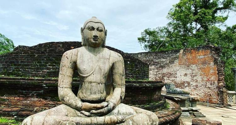 Oude stenen zittende Boeddhabeeldhouwwerk tussen bakstenen ruïnes en bomen in Polonnaruwa.