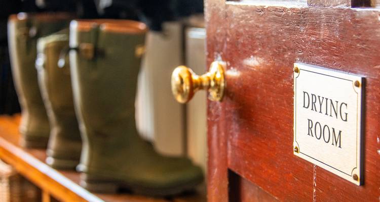 Primer plano de una puerta de madera con un letrero que dice 'Drying Room' y botas de goma borrosas detrás.