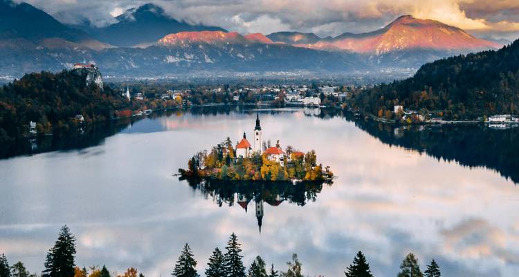 Vue aérienne spectaculaire du lac de Bled avec son église insulaire entourée de montagnes automnales au lever du soleil.