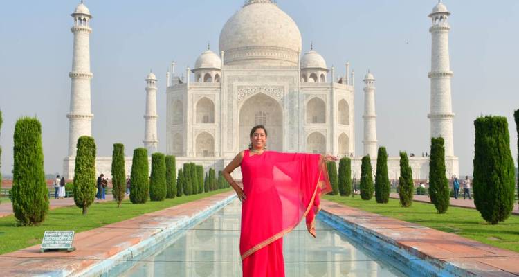 Frau in leuchtend farbigem Sari, die vor dem Spiegelbecken und dem Taj Mahal posiert