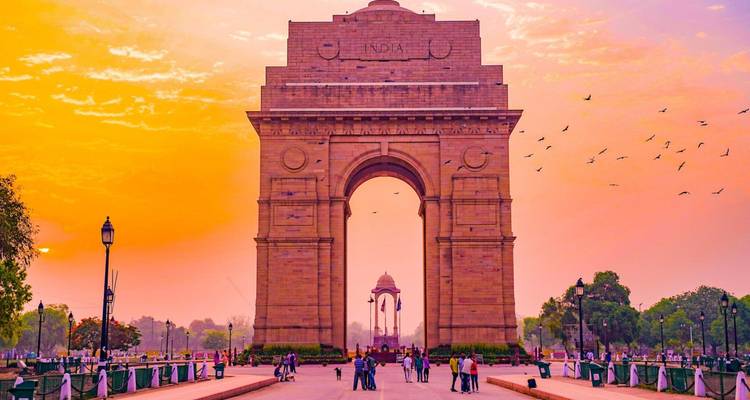 Das India Gate Denkmal leuchtet in warmen Sonnenaufgangstönen, während Besucher entlang der Promenade spazieren.
