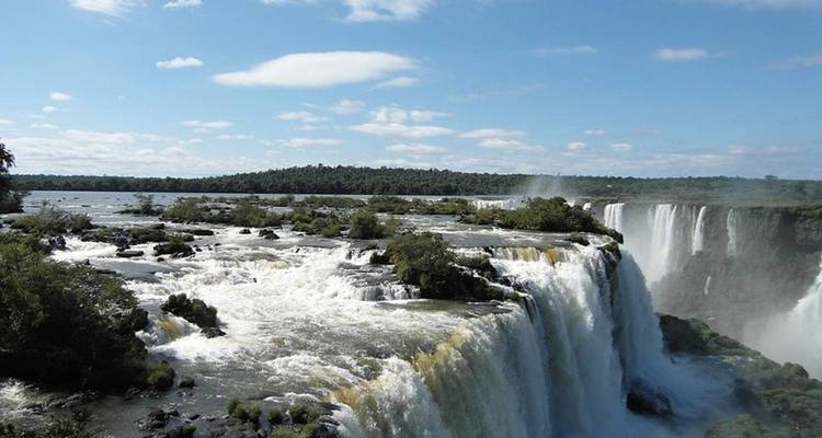 Vue latérale des chutes d'Iguazu avec de la brume s'élevant vers un ciel bleu dégagé.