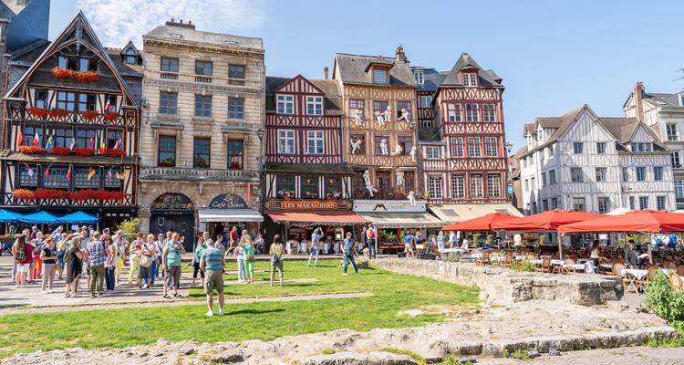 Place médiévale animée à Rouen bordée de bâtiments à colombages et en pierre, de balcons remplis de fleurs et de foules de touristes.